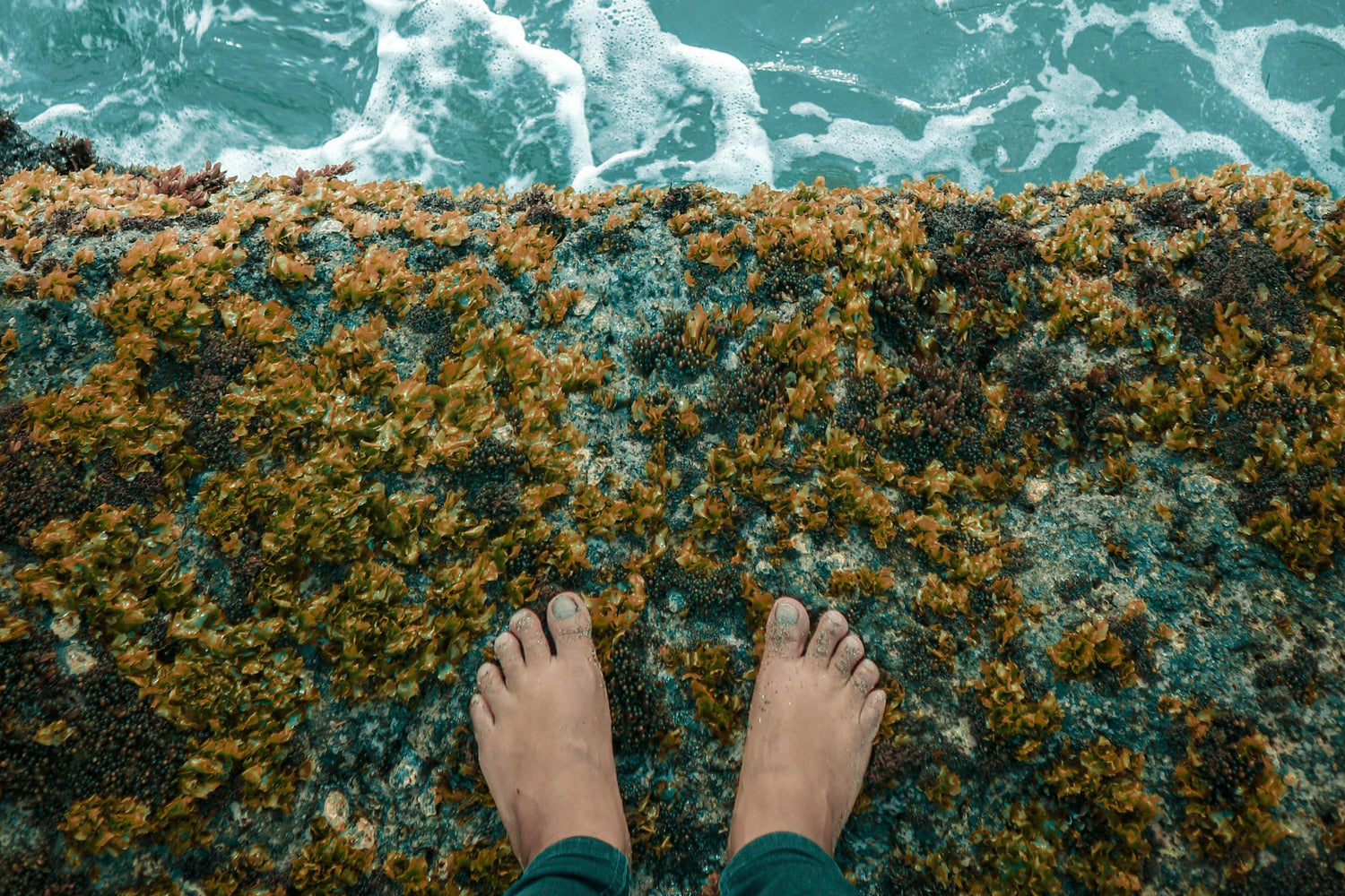 Feet standing on a rocky ledge with ocean waves crashing below